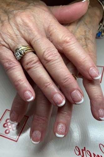 Classic white glitter french on short oval nails, older hands with large rings