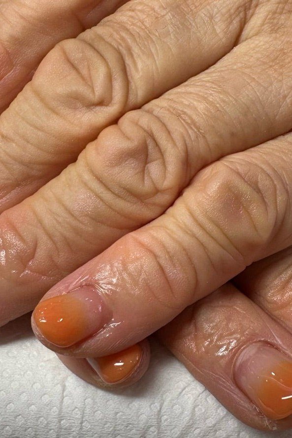 Burnt orange thermal ombre on short oval nails, mature hands
