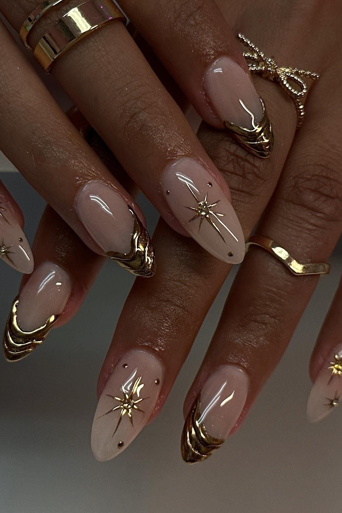 Nude almond nails with gold starburst art, dark-skinned hands