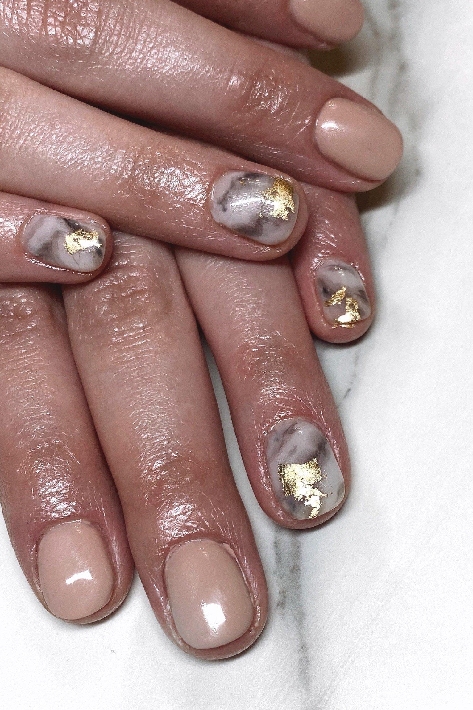 Nude nails with gold foil marble art, dark-skinned hands