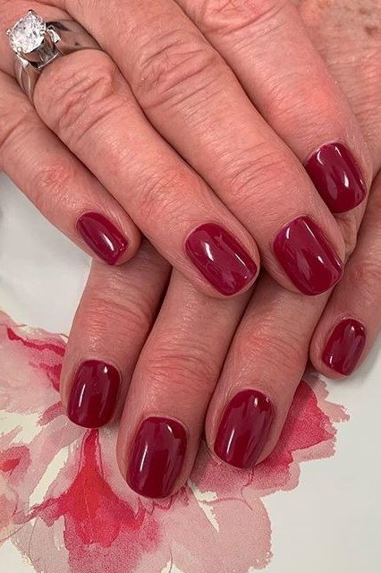 Wine-red glossy nails on mature hands with rings