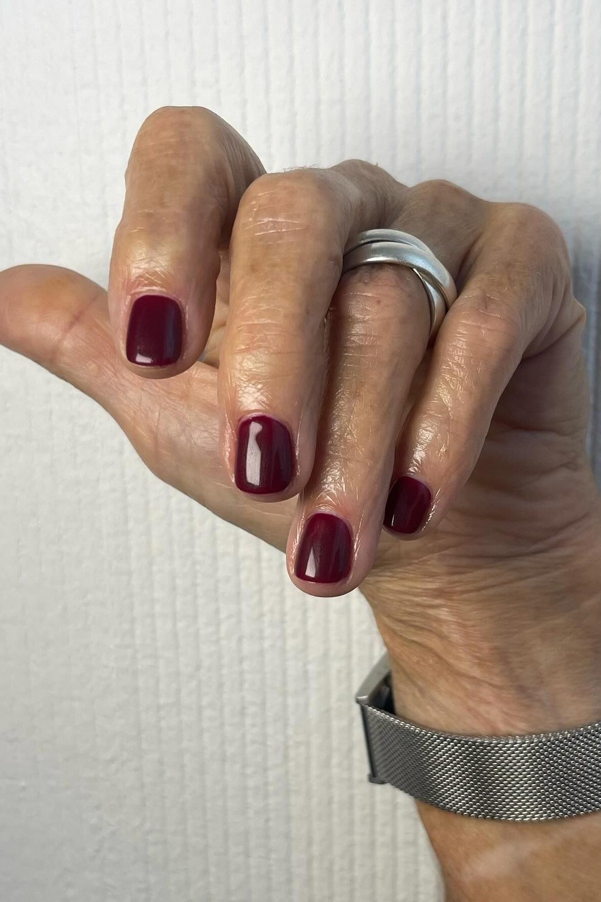 Rich burgundy polish on older hand with watch, short oval nails