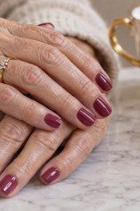Deep burgundy gloss nails on aged hands with tea setting