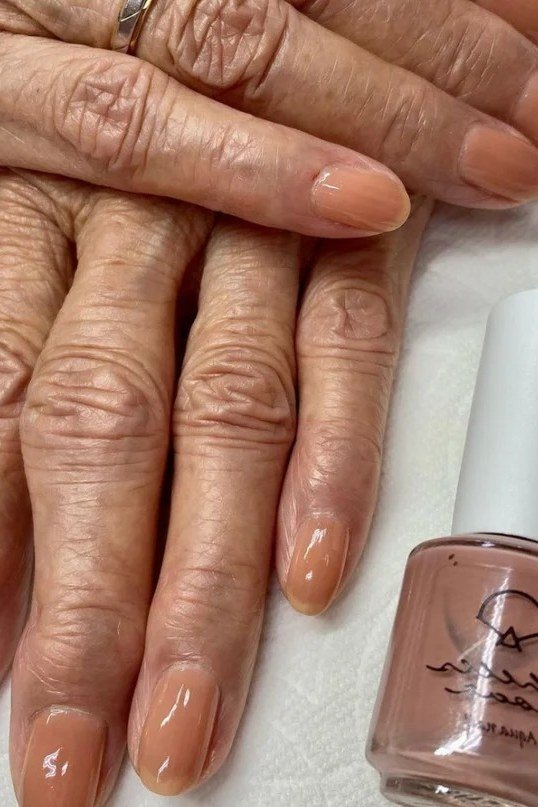 Nude taupe glossy nails with polish bottle on aged hands