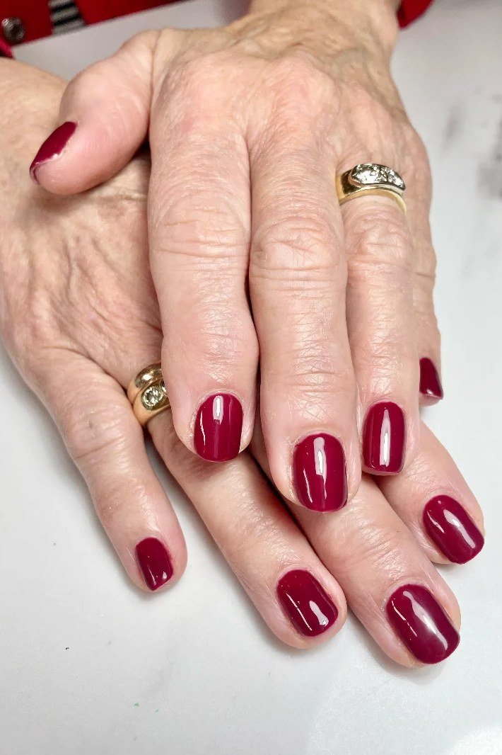 Burgundy red nails with bold gold ring for women over 60