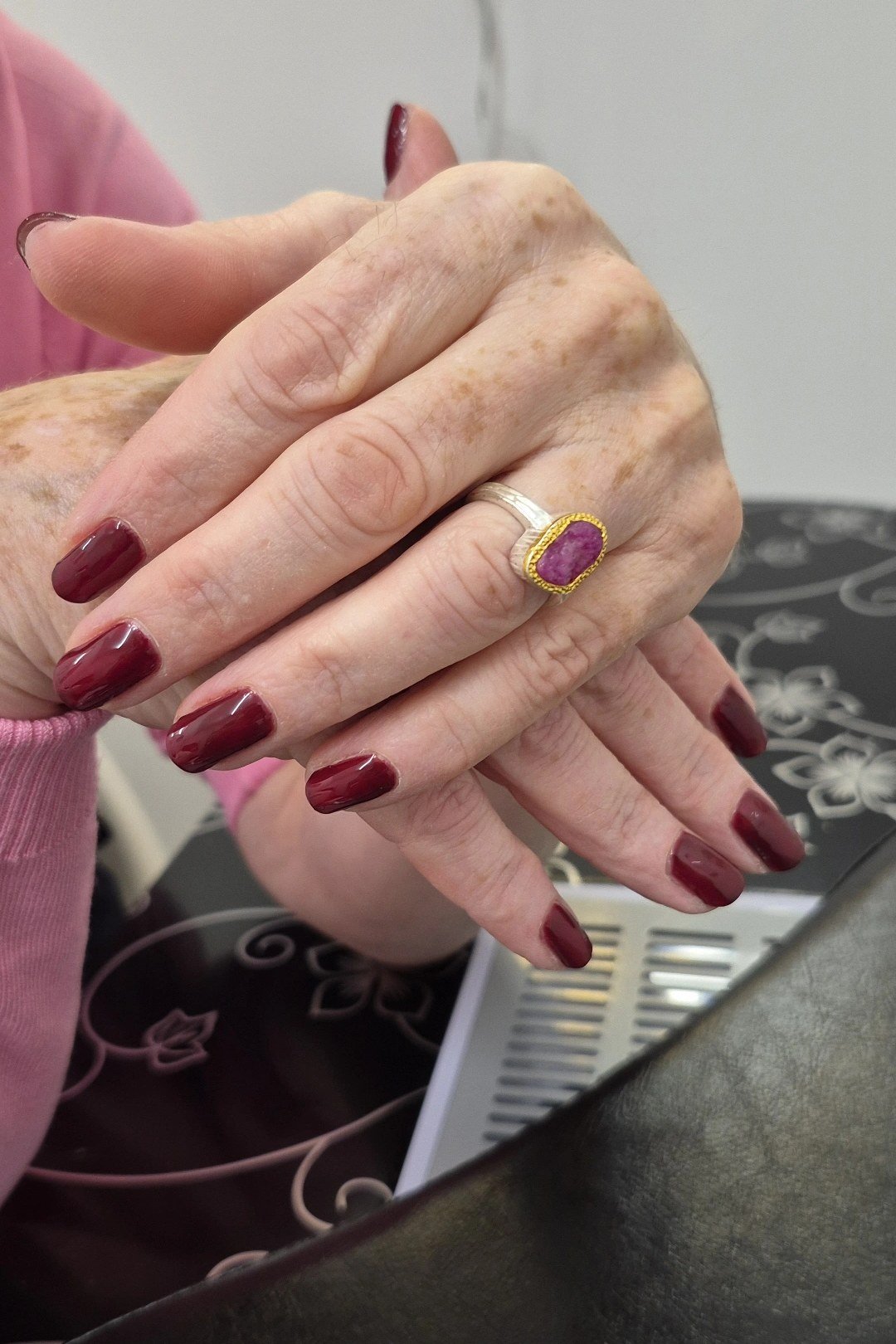 Burgundy red manicure on crossed hands with gold ring for women over 60