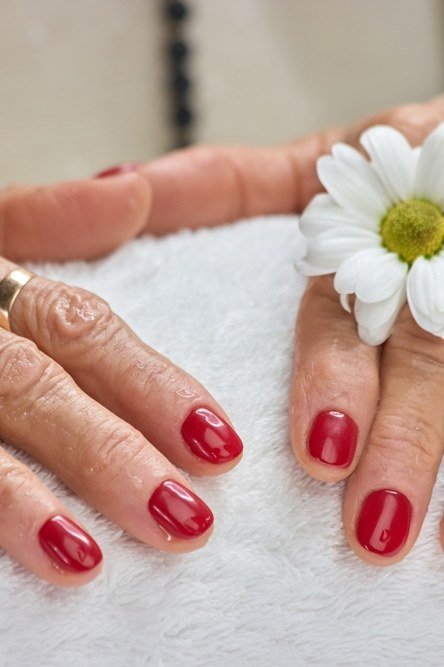 Cherry red nails with daisy flower on white towel for women over 60