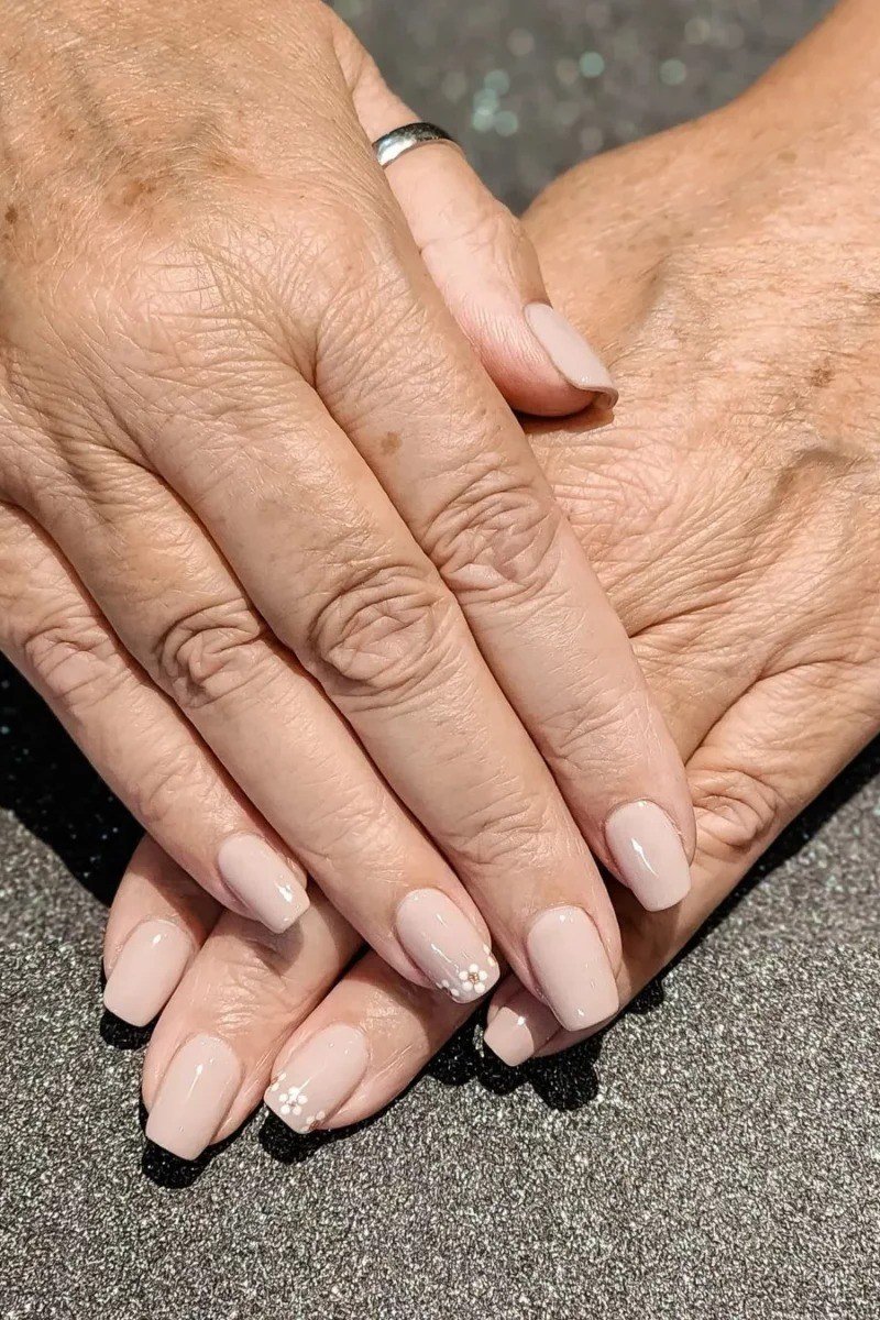 Elegant sheer pale nude nails on folded older hands for women over 40