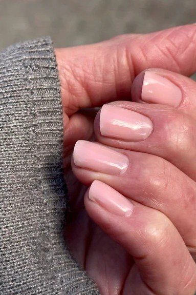 Elegant soft pink glossy nails against a grey sweater for women over 40