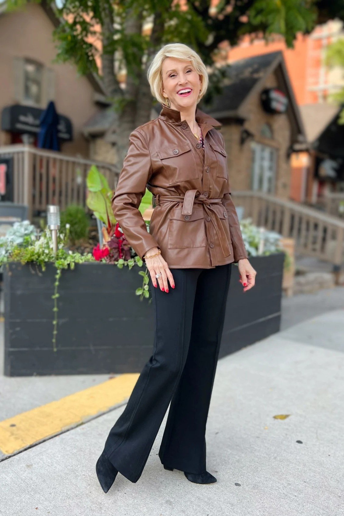 Woman over 40 wearing a cognac belted leather jacket with black wide-leg trousers
