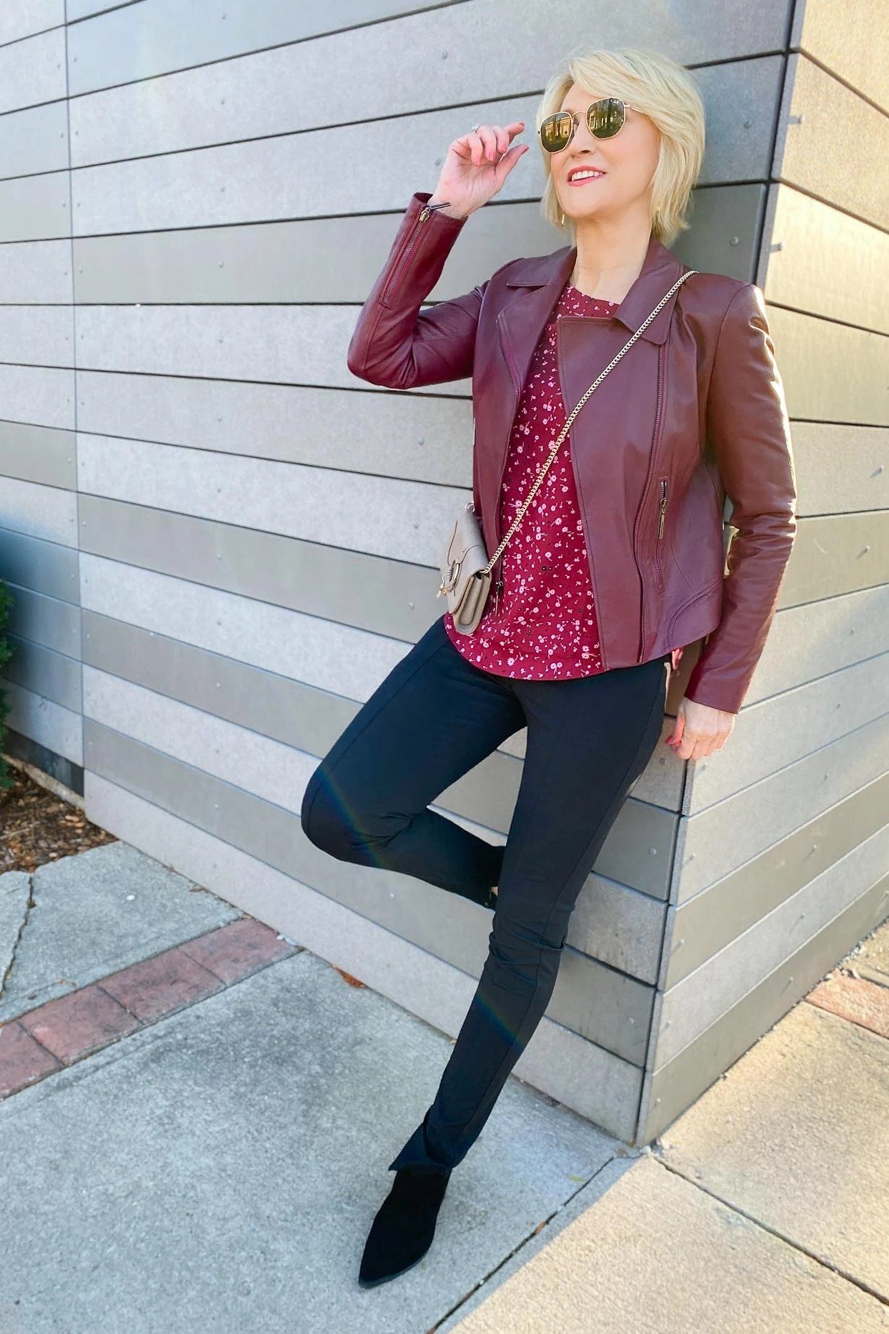 Woman over 40 wearing a burgundy moto jacket with a red polka-dot top and dark skinny jeans
