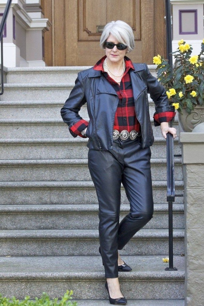 Woman over 40 wearing a black moto jacket over a red plaid shirt with leather-look pants
