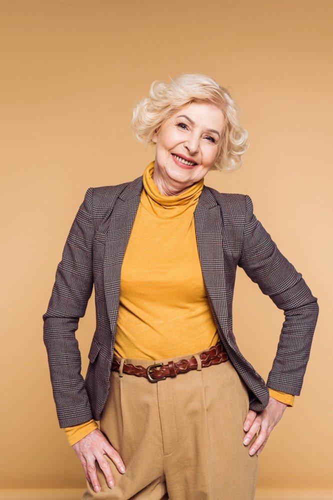 Woman over 40 wearing a gray blazer with a mustard turtleneck and tan trousers