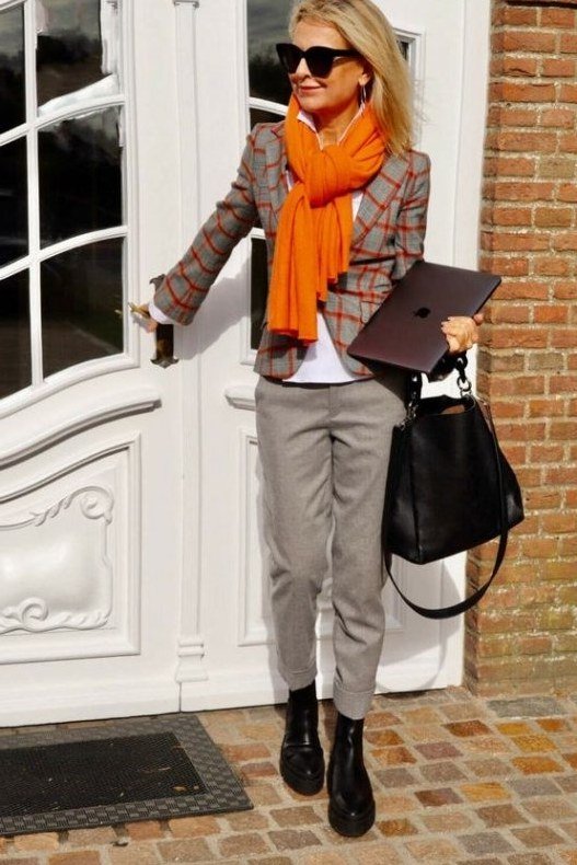 Woman over 40 wearing a plaid blazer with an orange scarf and gray trousers