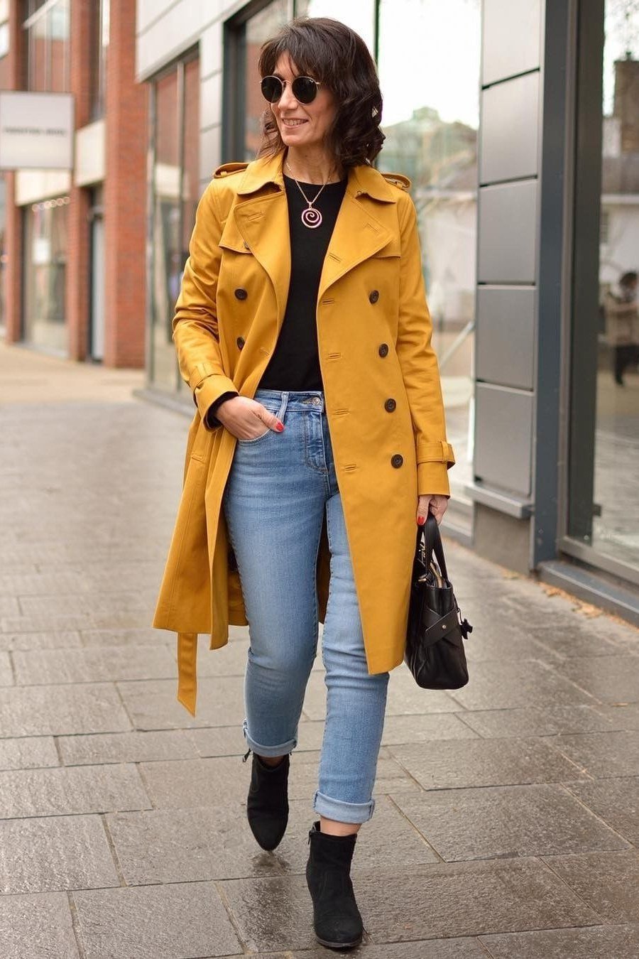 Woman over 40 wearing a mustard trench coat with a black top and skinny jeans
