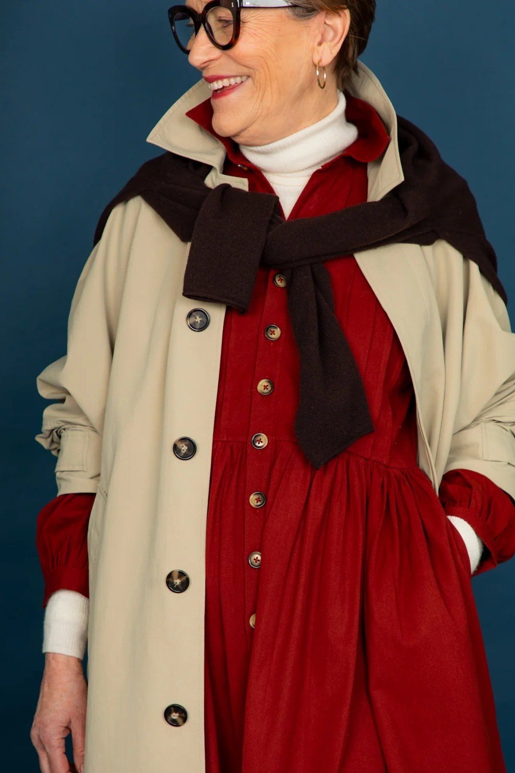 Woman over 40 wearing a beige trench coat layered over a red dress with a scarf