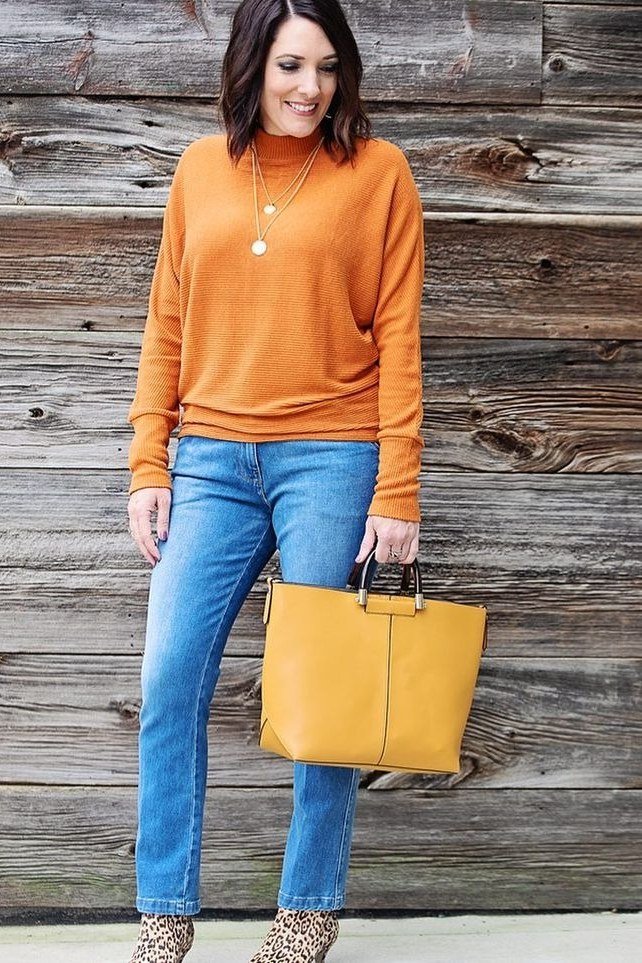 Woman over 40 wearing a mustard turtleneck with light-wash jeans and a yellow bag