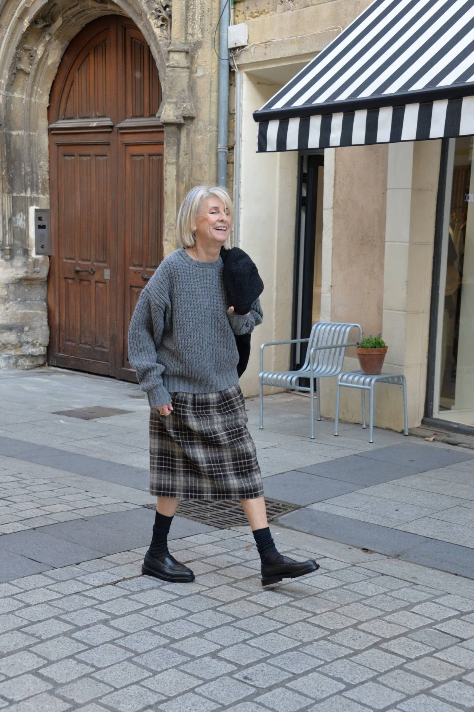 Woman over 40 wearing a gray oversized sweater with a plaid midi skirt