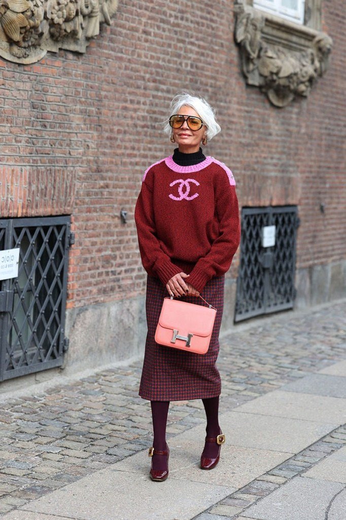 Woman over 40 wearing a red sweater with a burgundy midi skirt and pink bag