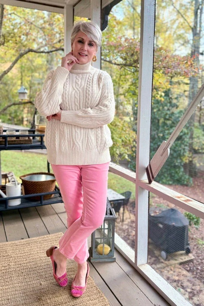 Woman over 40 wearing a cream cable sweater with pink trousers