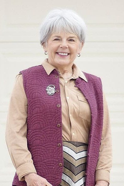 Woman over 40 wearing a magenta quilted vest over a tan shirt with a patterned midi skirt