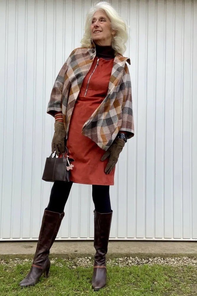 Woman over 40 wearing a rust sweater dress with a plaid shawl and knee boots