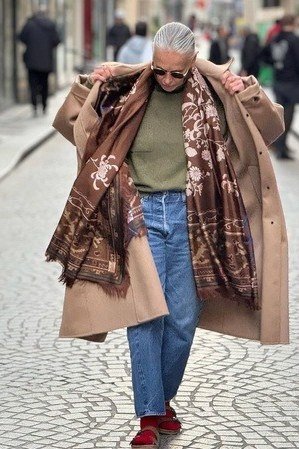 Camel coat over olive top and blue jeans with paisley scarf, timeless fall outfit for women over 60
