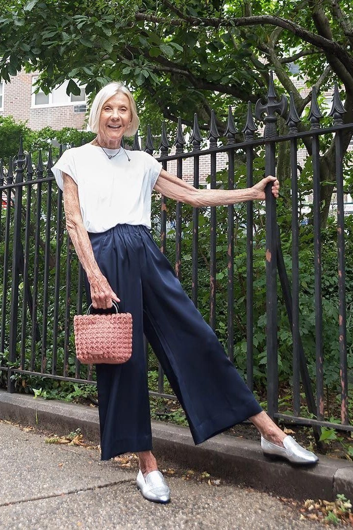 Effortlessly polished outfit for women over 50: A white tee tucked into navy wide-leg culottes, pink woven bucket bag, white...