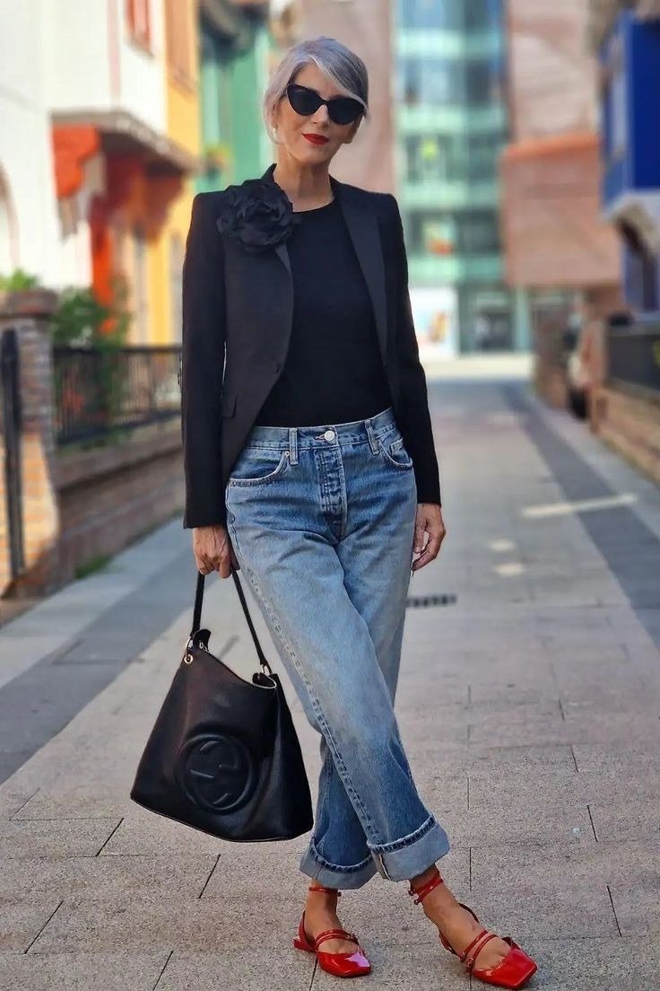 Effortlessly polished outfit for women over 50: A black blazer over a black top, cuffed medium-wash jeans, red strappy...