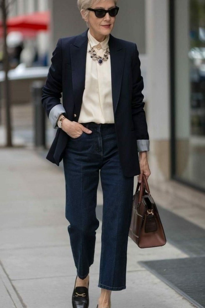 Effortlessly polished outfit for women over 50: A navy blazer over an ivory shirt, navy tailored trousers, brown leather tote