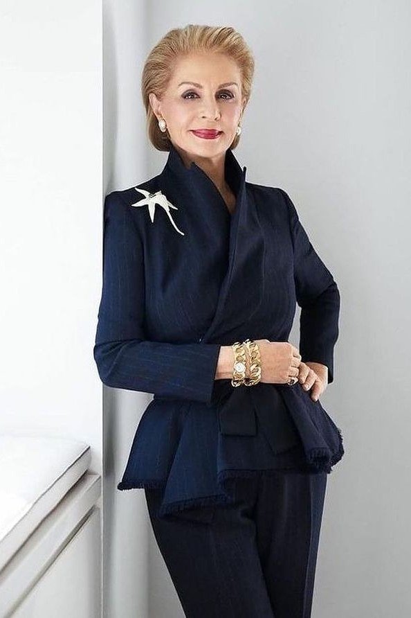 Effortlessly polished outfit for women over 50: A navy blazer with a white floral brooch and navy trousers, gold bracelets