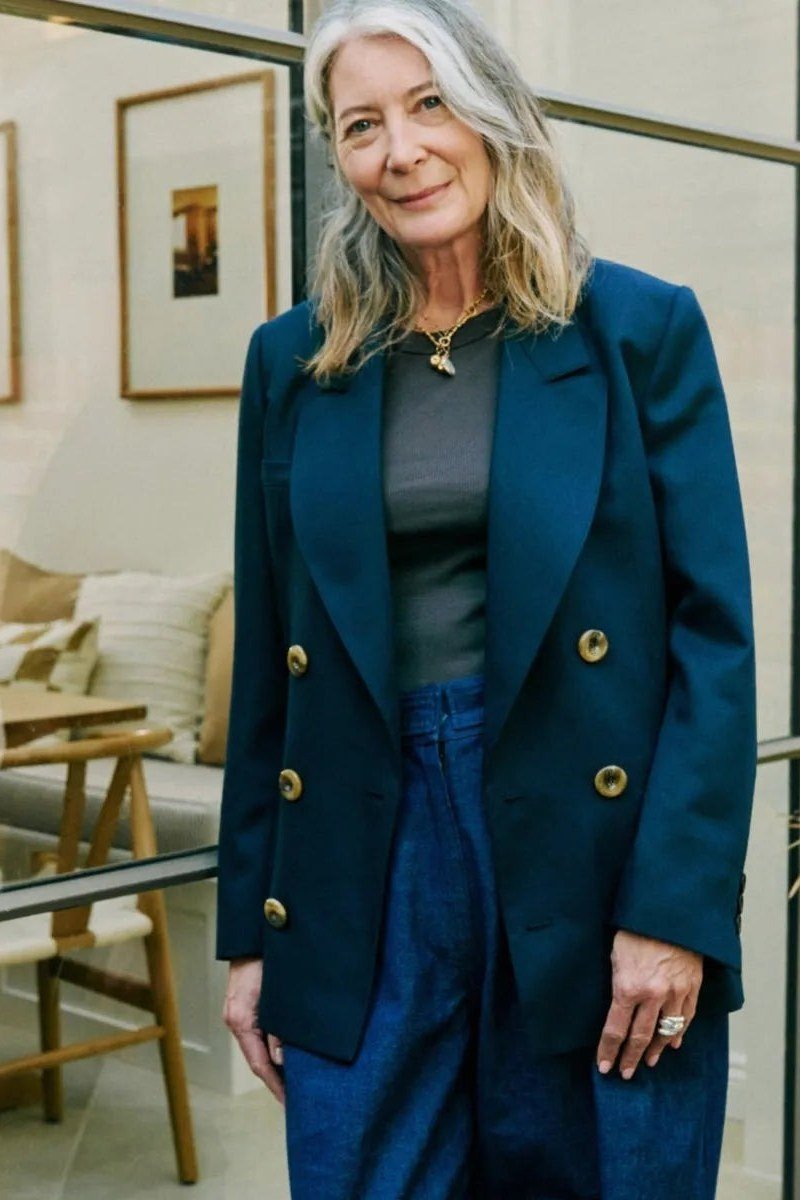 Effortlessly polished outfit for women over 50: A teal double-breasted blazer with gold buttons over a gray top and blue...