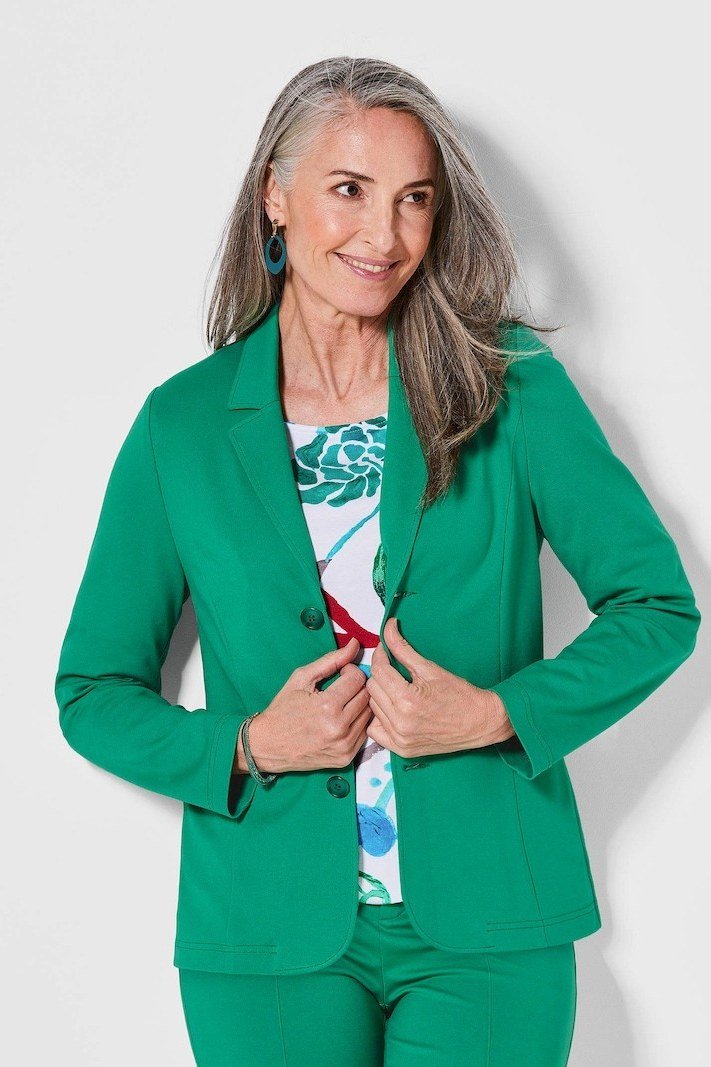 Effortlessly polished outfit for women over 50: An emerald green tailored suit with a patterned blouse, seated