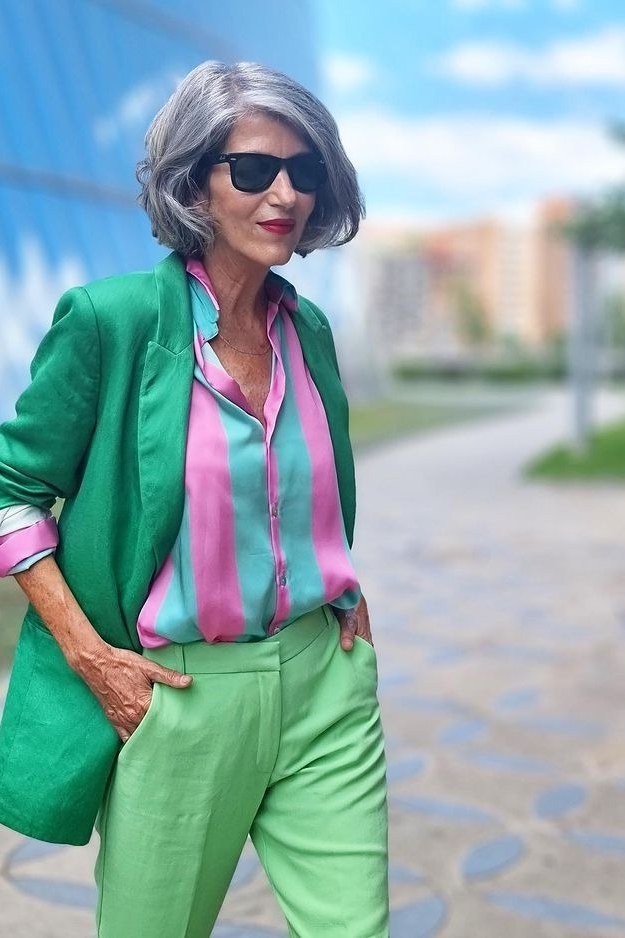 Effortlessly polished outfit for women over 50: A green blazer over a pink-and-blue striped shirt and green trousers