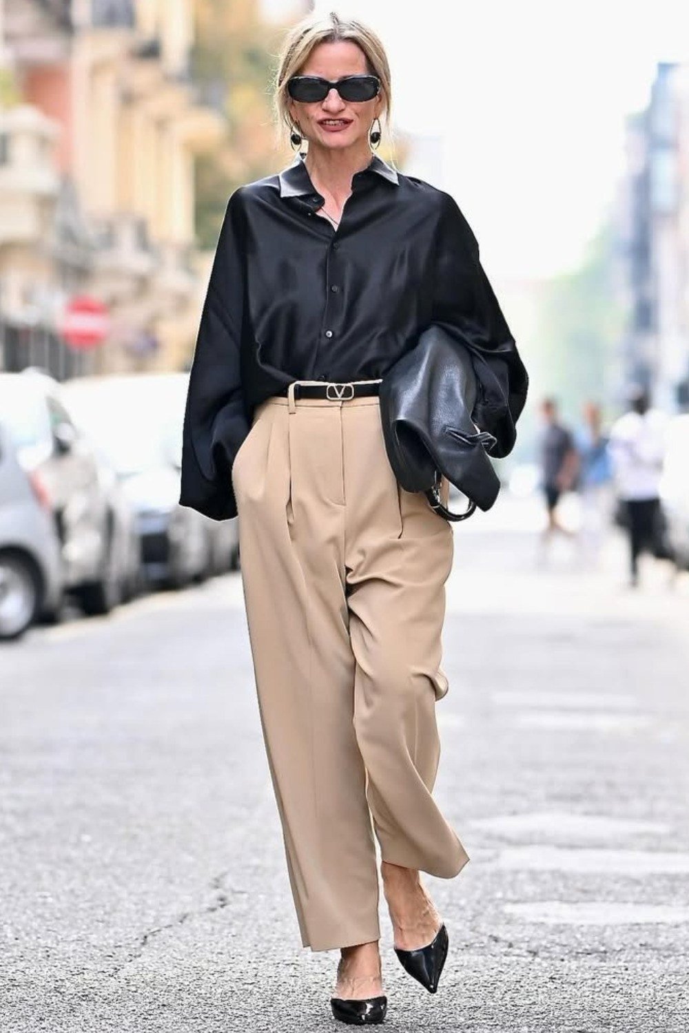 Effortlessly polished outfit for women over 50: A navy silk blouse and camel wide-leg trousers, black flats, black shoulder...