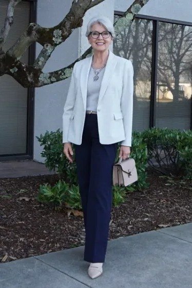Woman over 70 wearing a white blazer with navy slim pants and white sneakers, smart casual look