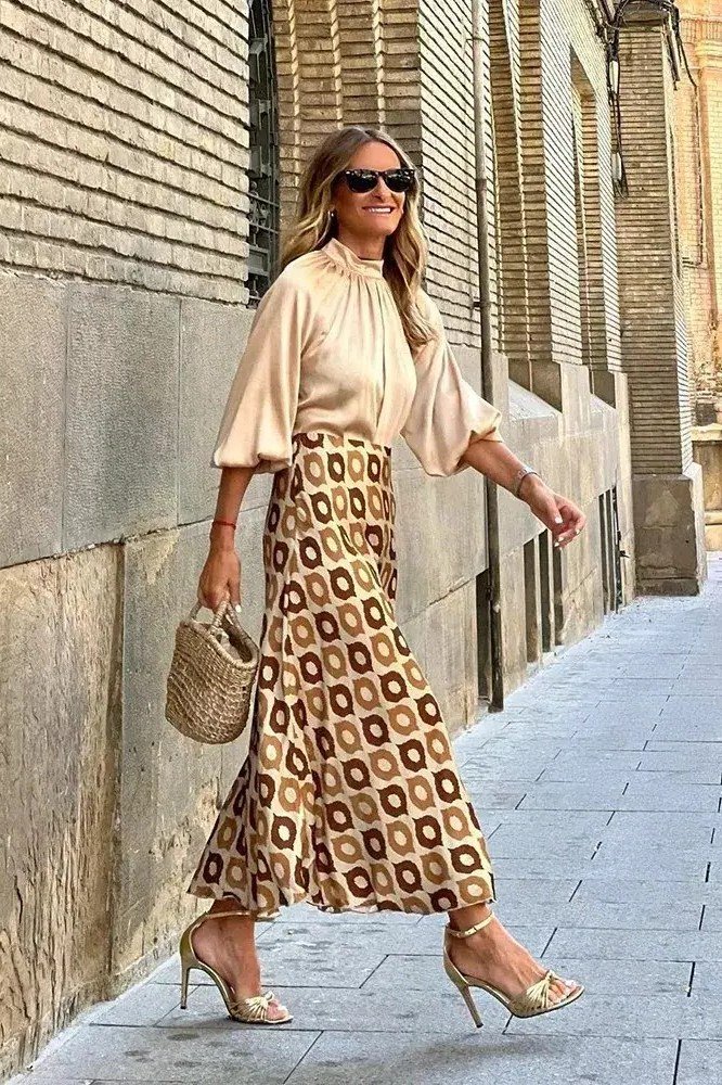 Older woman wearing a printed cream blouse with mustard midi skirt and gold heels, chic outfit for women over 70