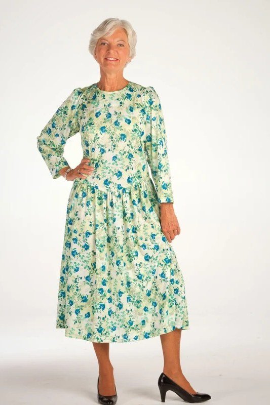 Woman over 70 wearing a green floral midi dress with long sleeves and black heels, dressy outfit for older women