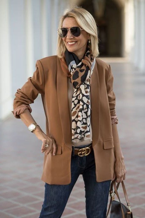Older woman wearing a camel blazer with leopard print scarf and dark jeans, bold casual outfit for women over 70