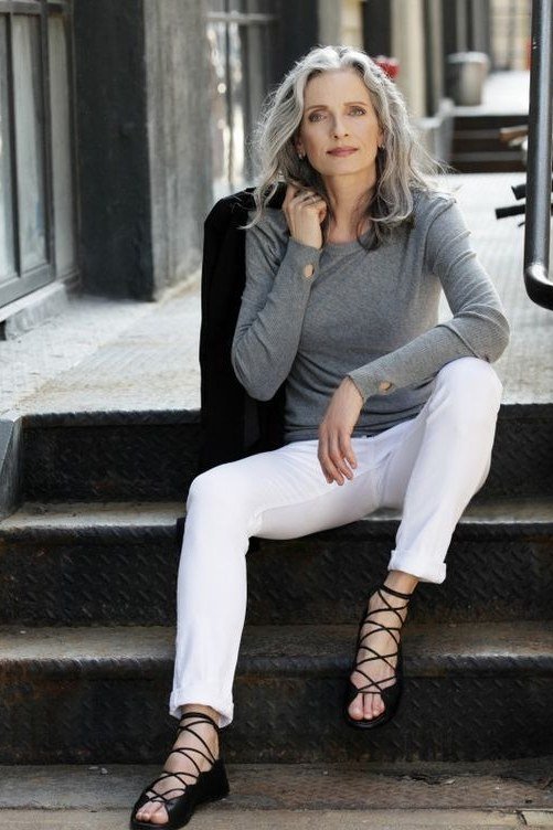 Older woman in a gray top and white pants sitting on city steps, casual outfit idea for women over 70