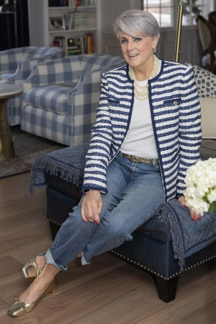 older woman sitting indoors in a navy striped cardigan and jeans, casual outfit for women over 70