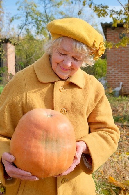 october outfits for women over 60: mustard coat beret holding large pumpkin garden