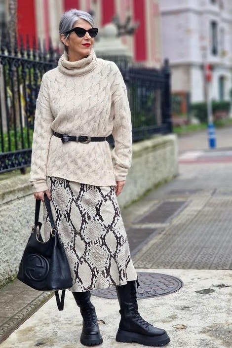 october outfits for women over 60: woman over 60 in cream cable turtleneck, snakeskin midi skirt and black boots on city street