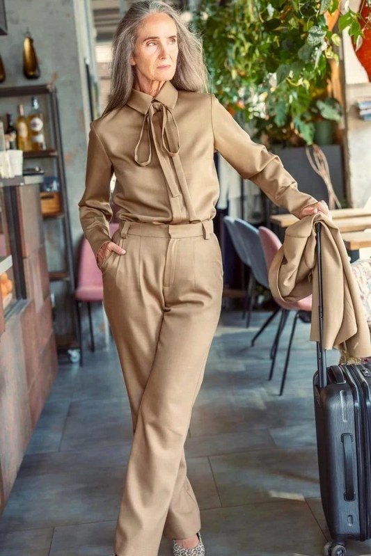 Trendy outfit for women over 70: camel blouse + camel wide-leg with suitcase