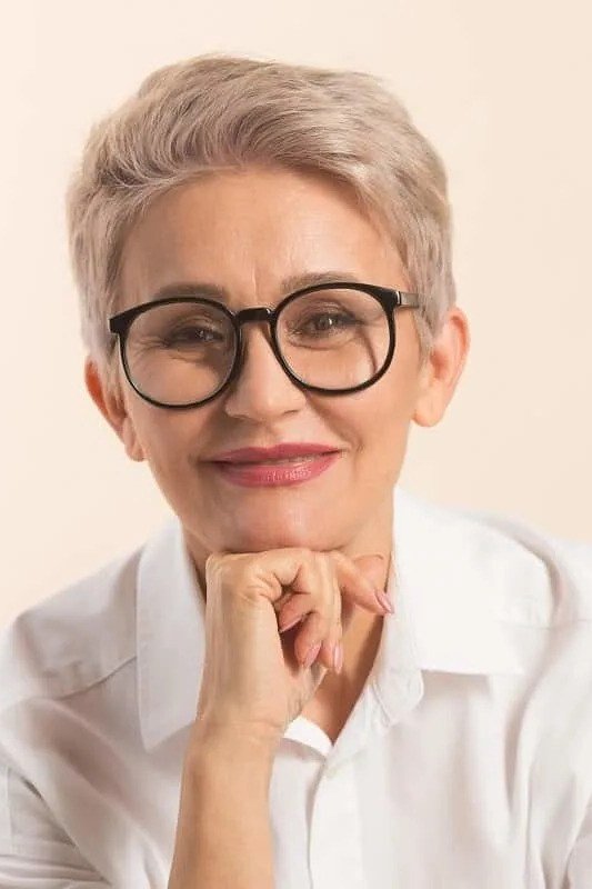 Blonde pixie with black round glasses, front view - pixie haircut for women over 60