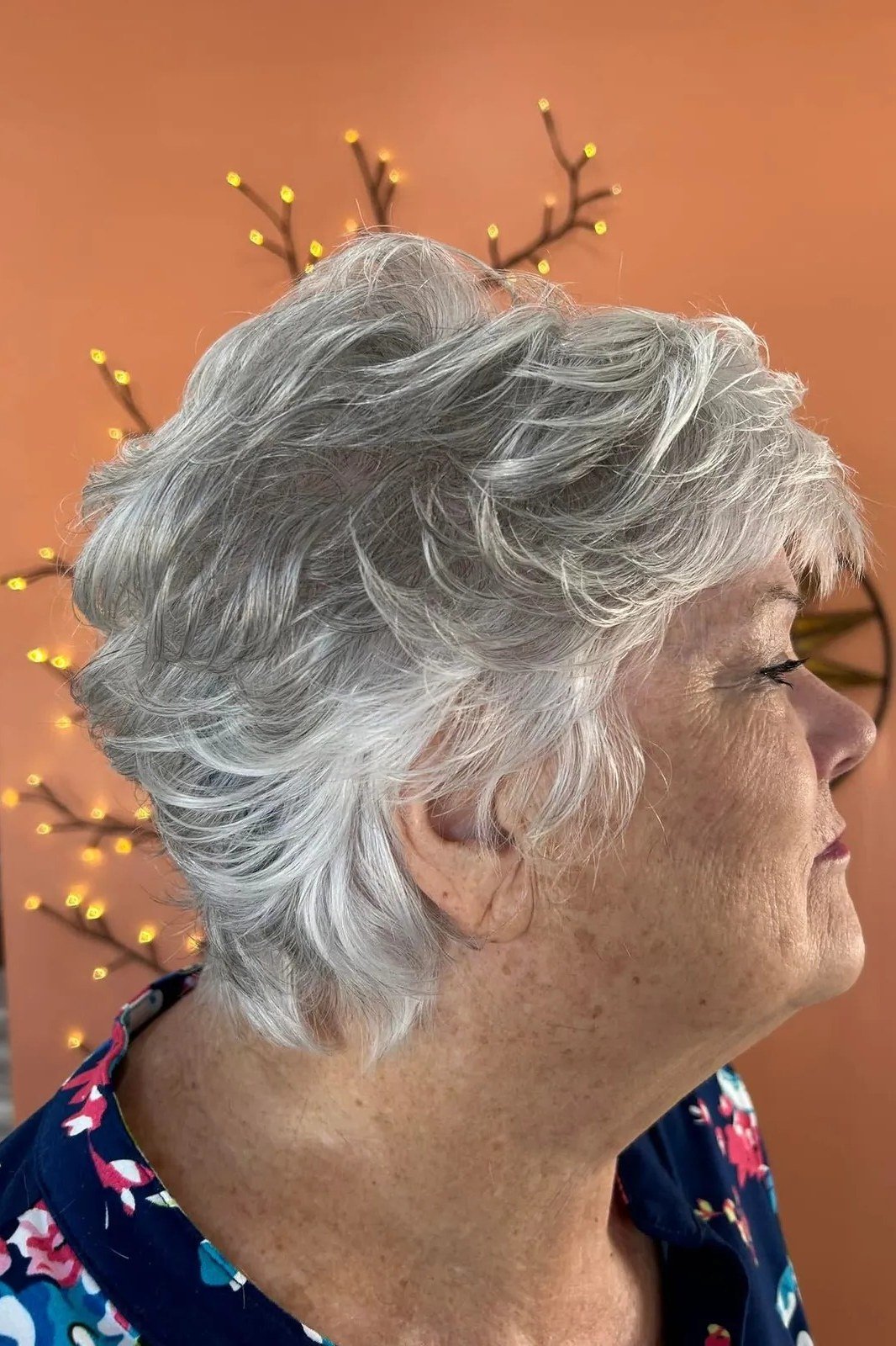 Grey curly pixie haircut with side bangs, profile view, for women over 60