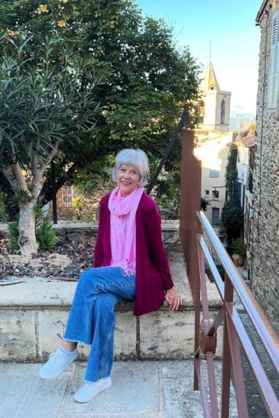 plus-size older woman wearing magenta cardigan, pink scarf and bright blue jeans