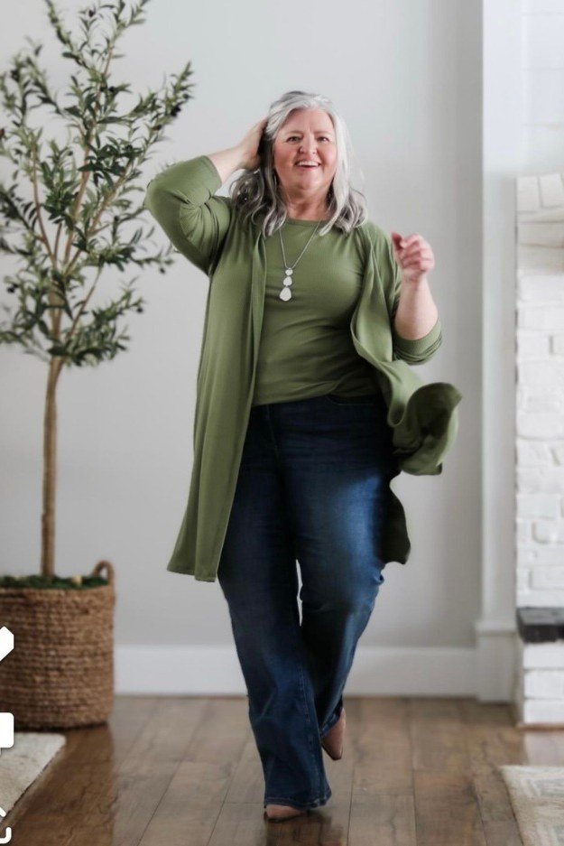 curvy woman over 60 wearing olive longline cardigan and dark jeans indoors