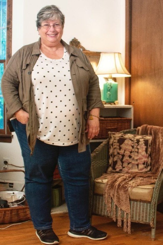 plus-size woman over 60 wearing polka-dot blouse and olive utility jacket with jeans