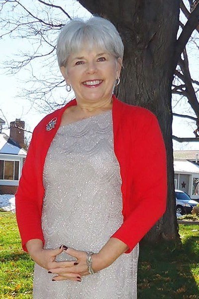 older woman over 60 wearing red cardigan over silver-grey top outdoors